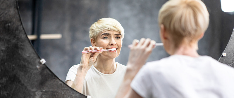 woman brushing teeth in mirror